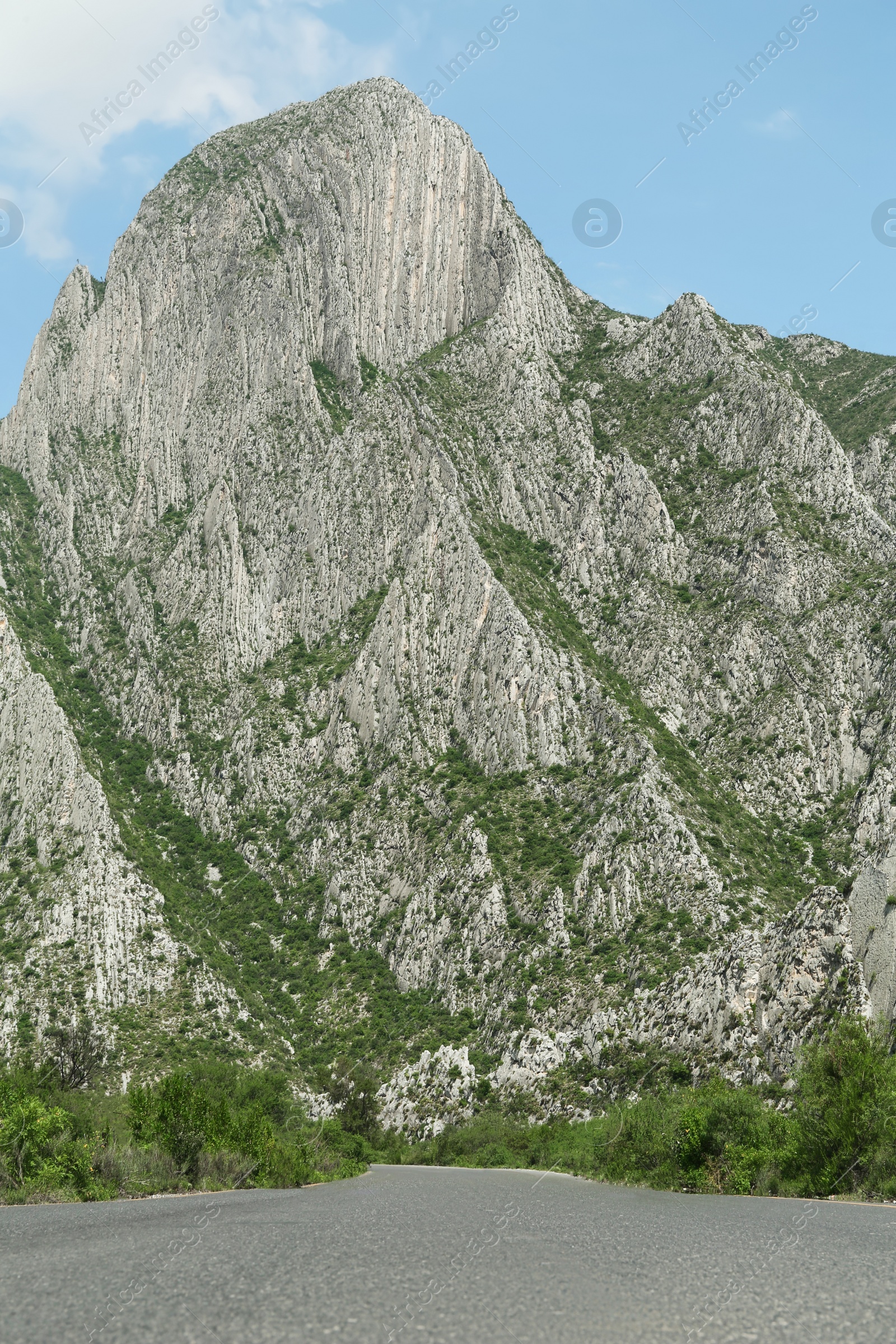 Photo of Picturesque view of big mountains and bushes near road under bright sky