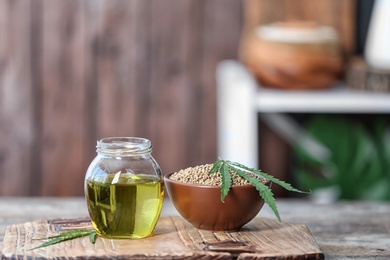 Jar with hemp oil and bowl of seeds on wooden table