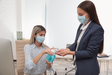 Photo of Office employees in respiratory masks applying hand sanitizer at workplace