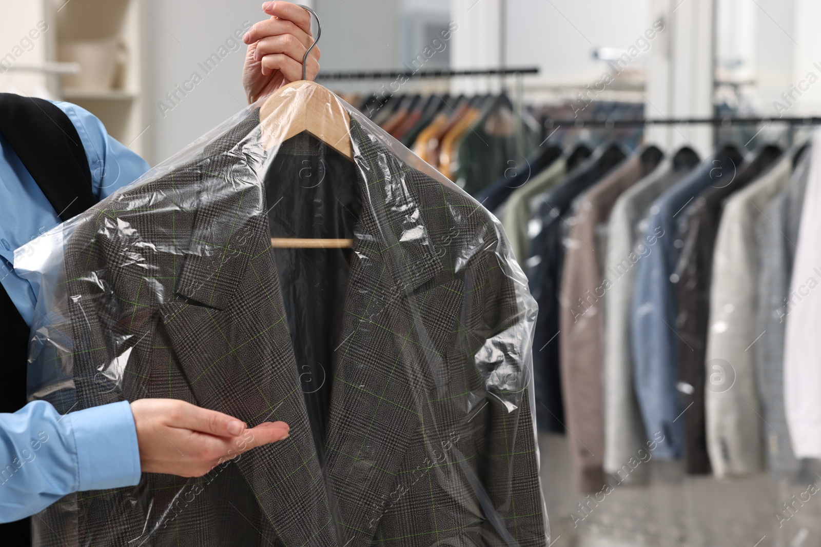 Photo of Dry-cleaning service. Woman holding jacket in plastic bag indoors, closeup and space for text