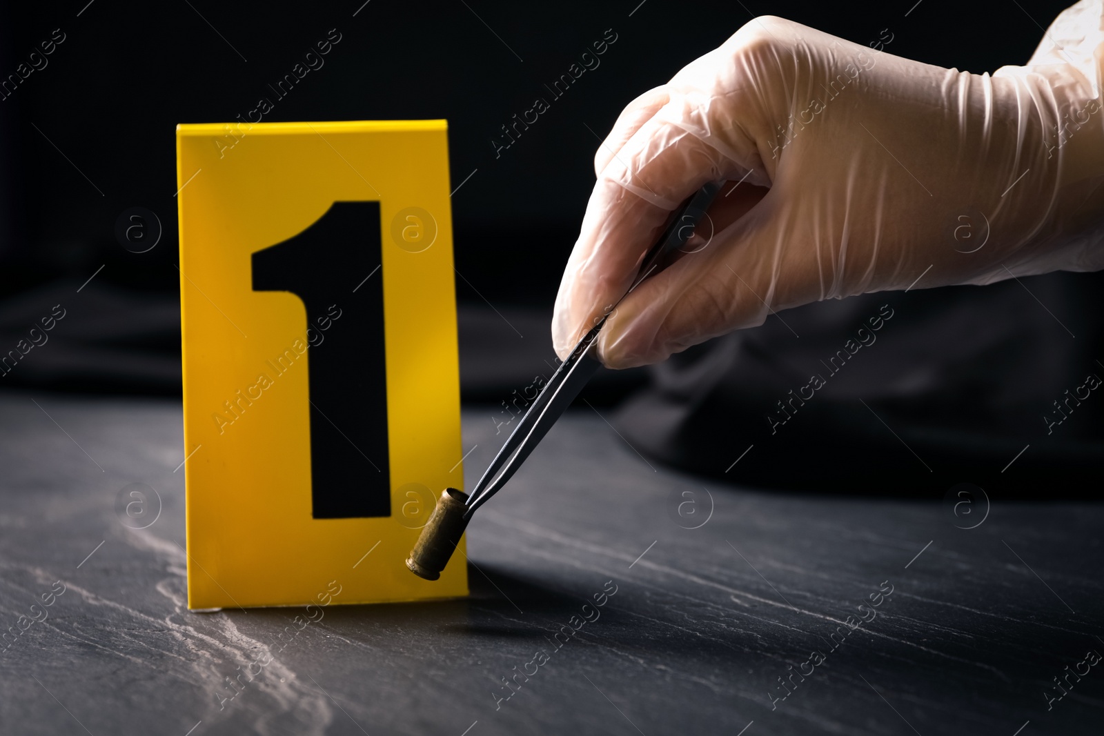 Photo of Woman taking shell casing near evidence marker at black slate table, closeup. Crime scene