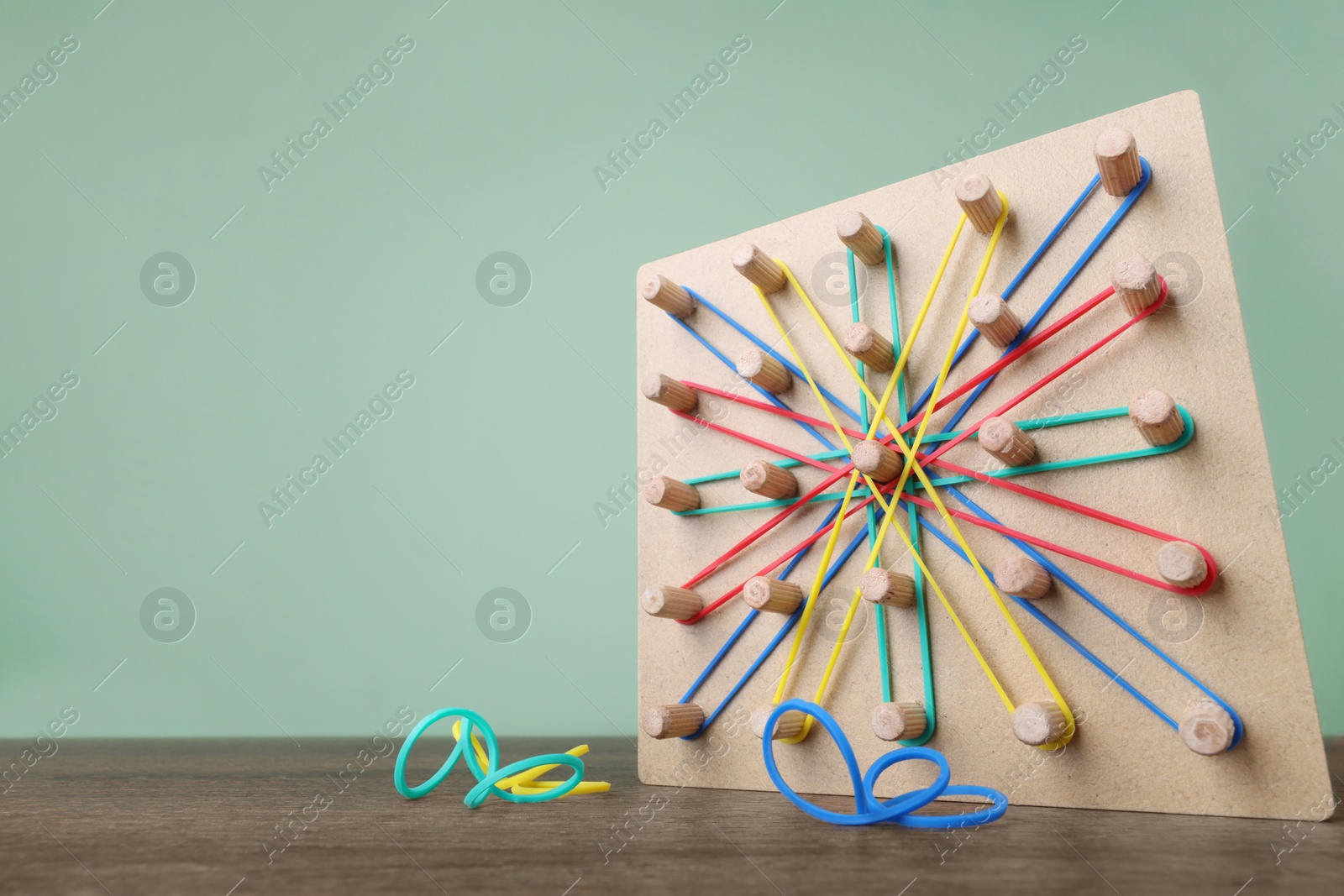 Photo of Wooden geoboard and rubber bands on table against grey wall, low angle view with space for text. Motor skills development