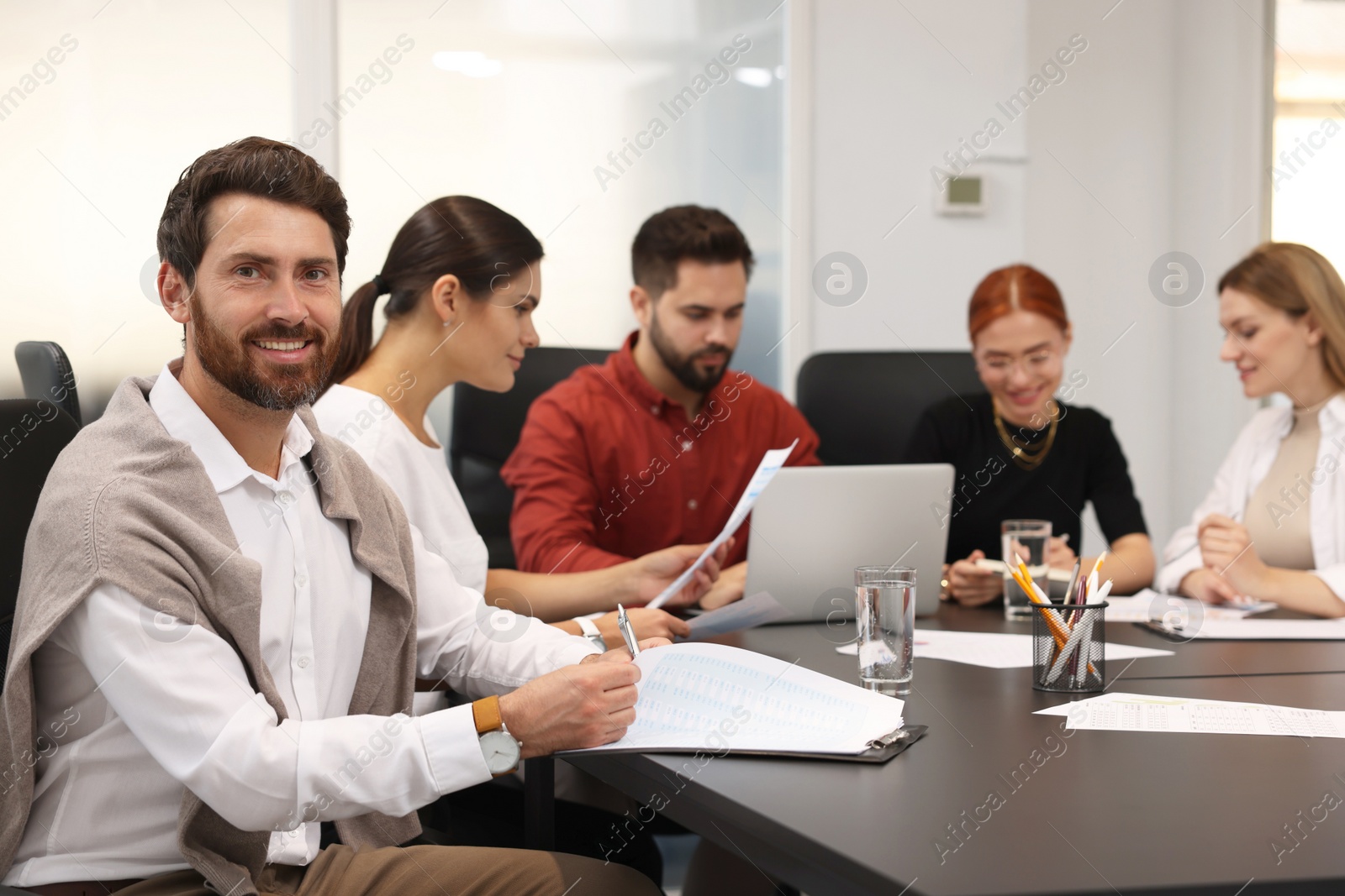 Photo of Team of employees working together in office. Happy man at table indoors