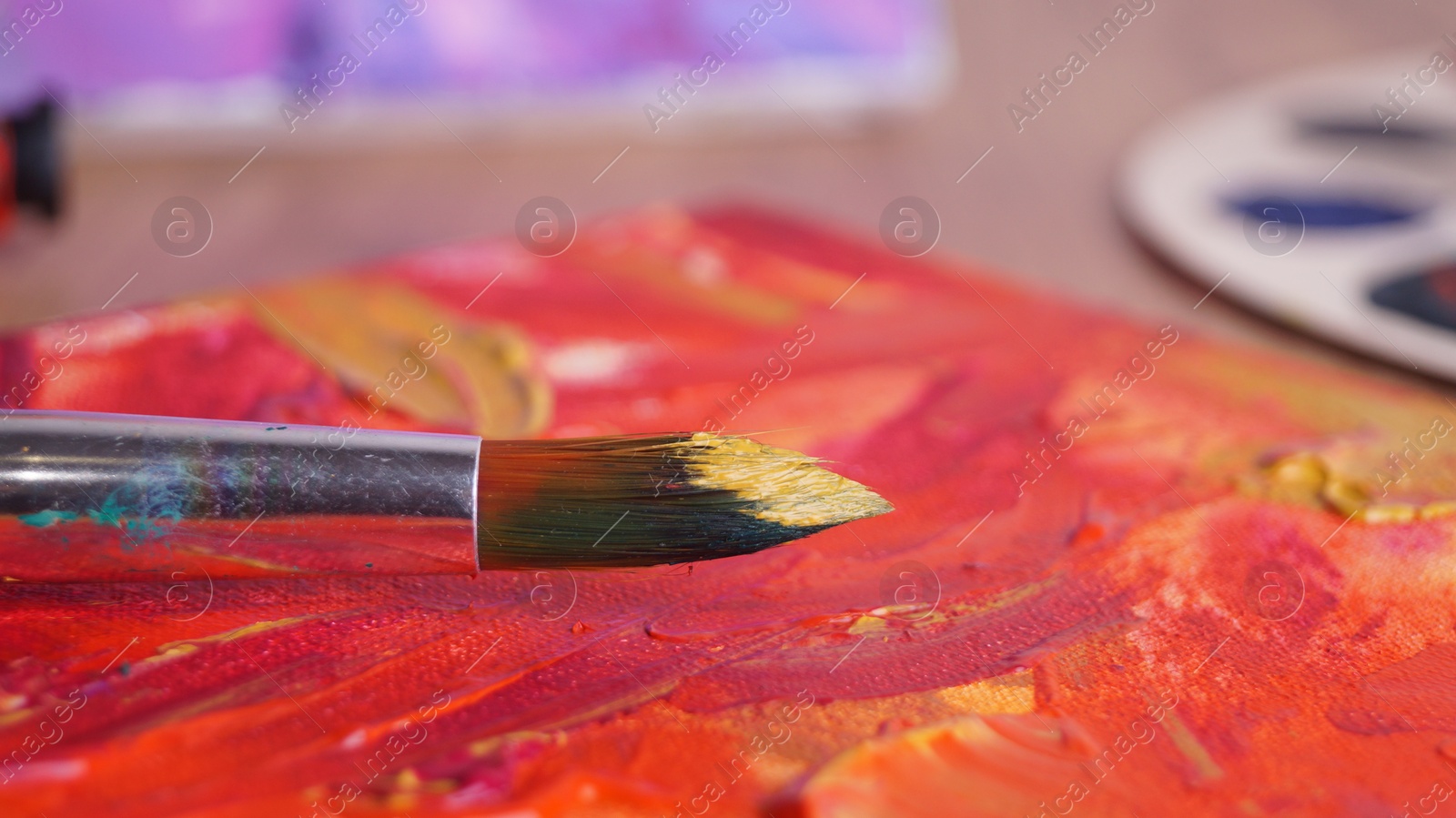 Photo of Artist's canvas with mixed paints and brush on table, closeup