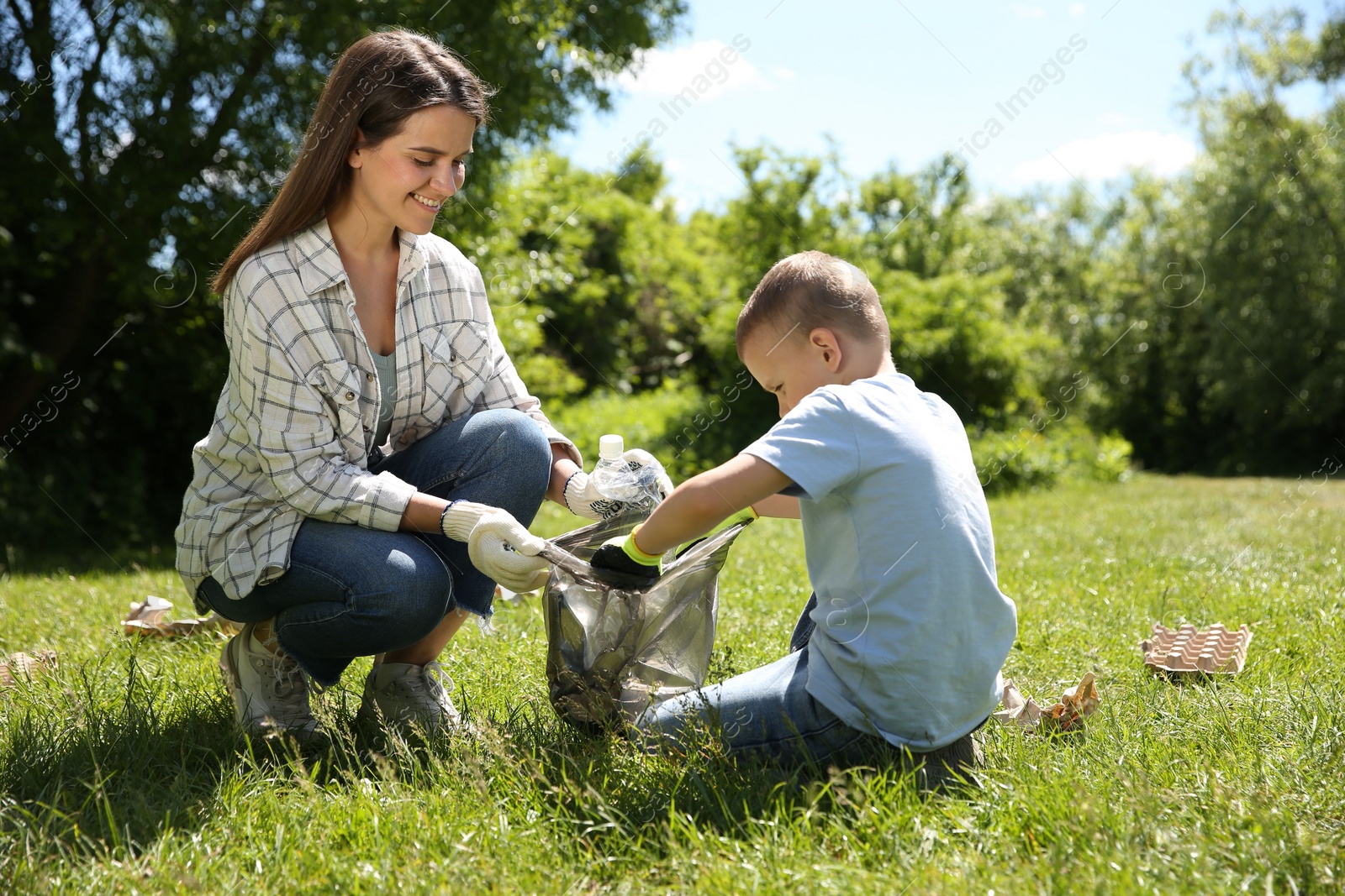 Photo of Mother and her son with plastic bag collecting garbage in park