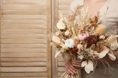 Photo of Woman holding beautiful dried flower bouquet on wooden background, closeup. Space for text