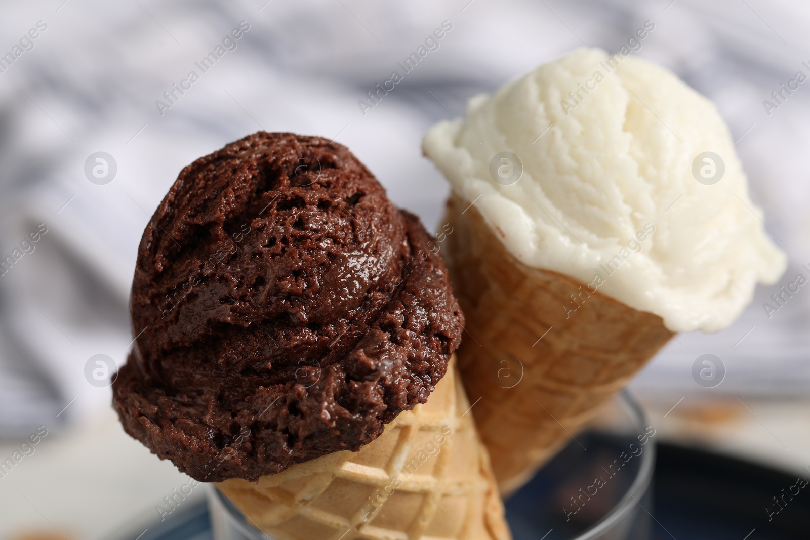 Photo of Tasty ice cream scoops in waffle cones on blurred background, closeup