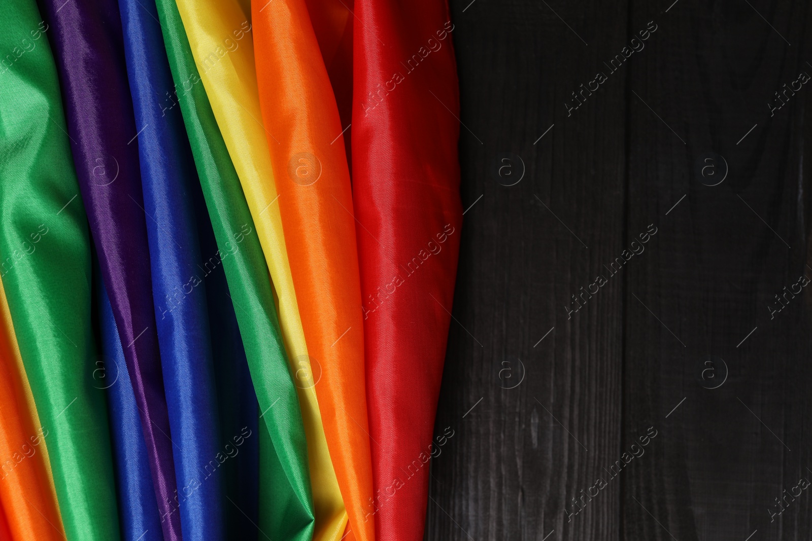 Photo of Rainbow LGBT flag on black wooden background, top view. Space for text