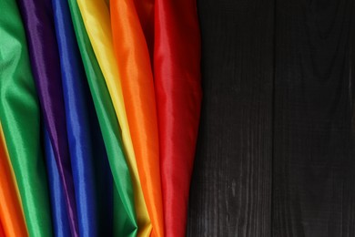 Photo of Rainbow LGBT flag on black wooden background, top view. Space for text