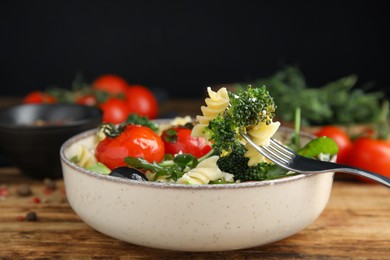 Photo of Bowl of delicious pasta with tomatoes, broccoli and cheese on wooden table, closeup