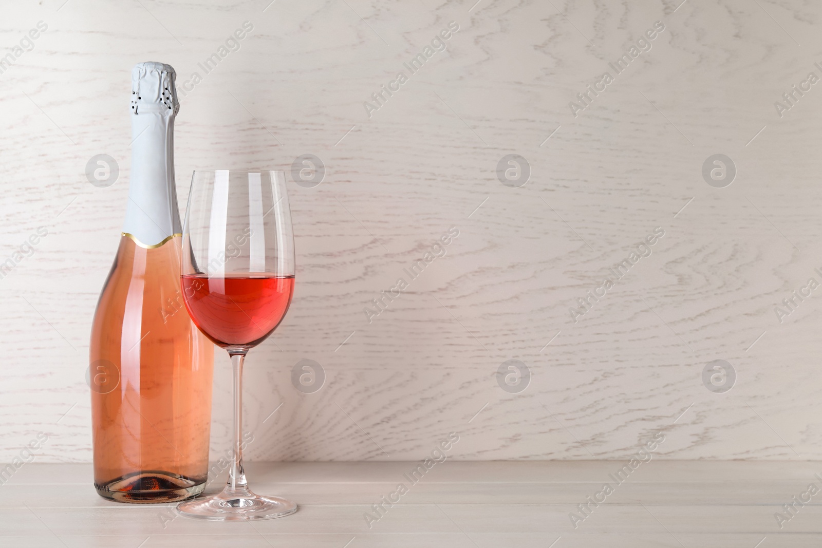 Photo of Bottle and glass of delicious rose wine on table against white wooden background. Space for text