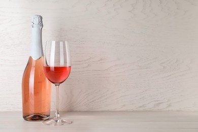 Bottle and glass of delicious rose wine on table against white wooden background. Space for text