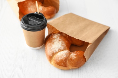 Photo of Cup of coffee and pastry in paper bags on wooden table