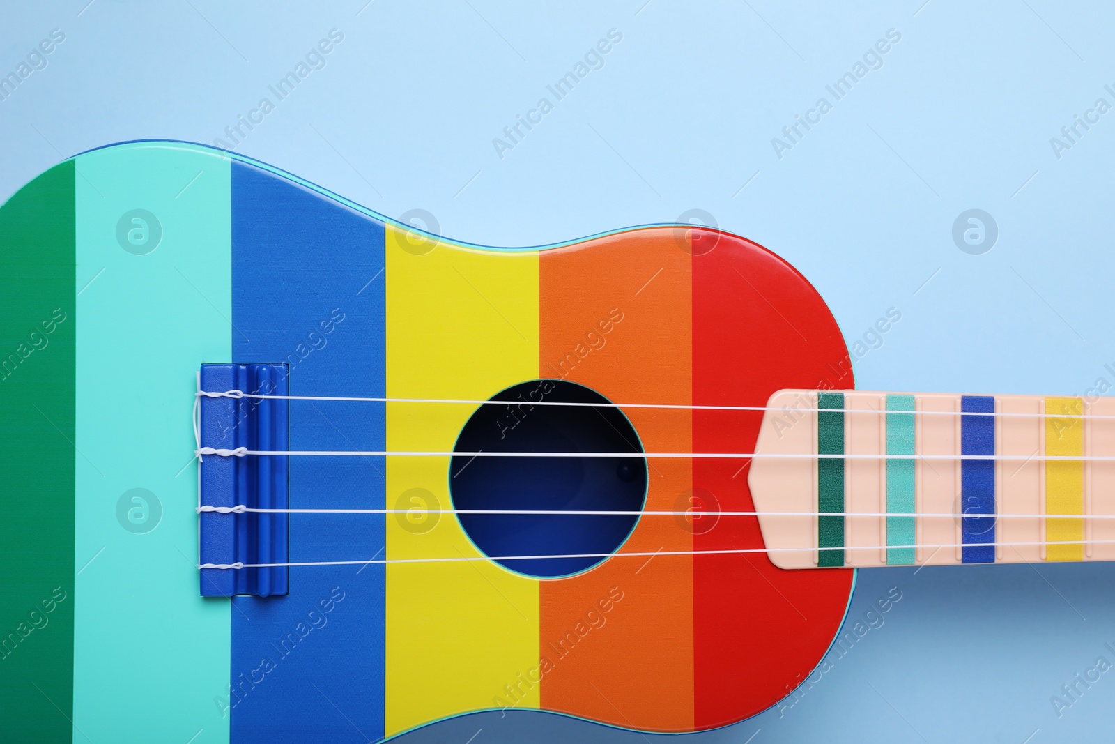 Photo of Colorful ukulele on light blue background, top view. String musical instrument