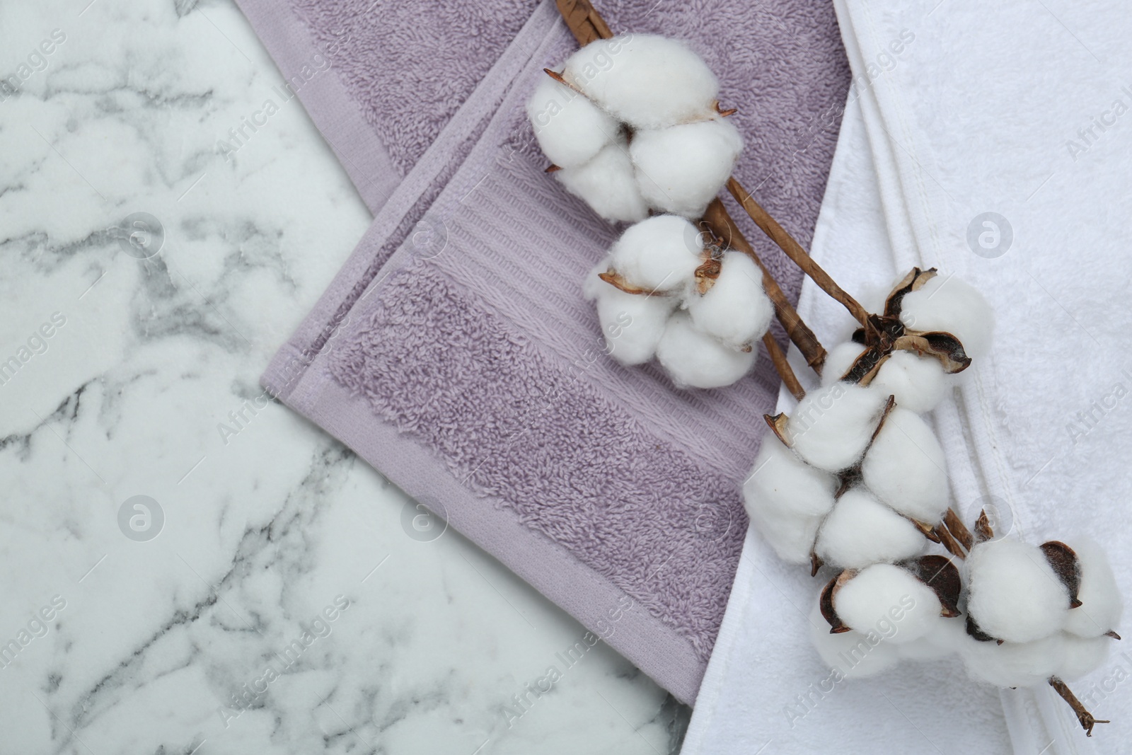 Photo of Different terry towels and cotton flowers on white marble table, flat lay. Space for text