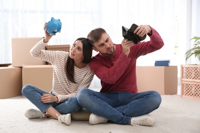 Photo of Unhappy young couple with empty piggy bank and wallet at home. Money problems