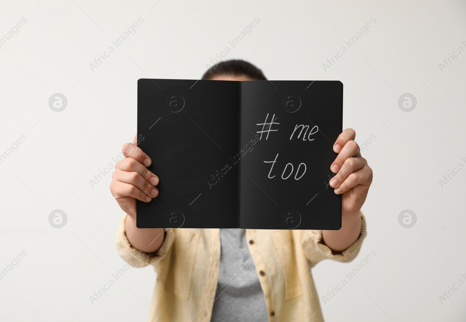 Photo of Woman holding notebook with hashtag MeToo against light background, closeup. Stop sexual assault