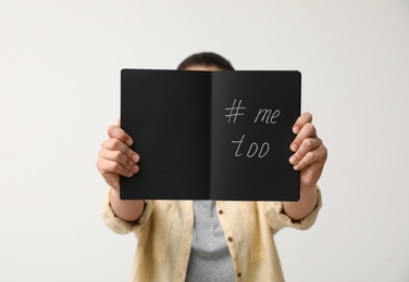 Photo of Woman holding notebook with hashtag MeToo against light background, closeup. Stop sexual assault