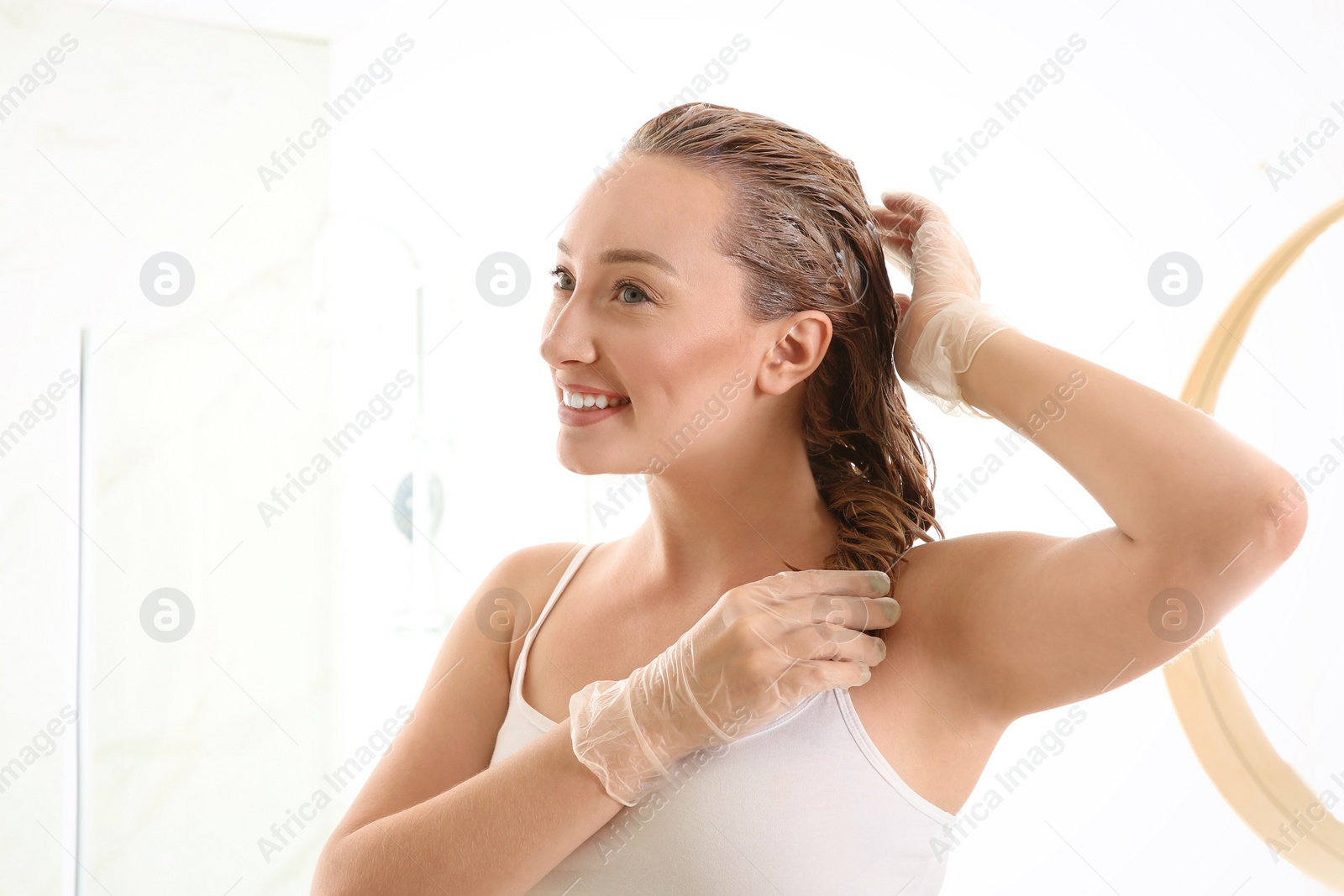 Photo of Young woman dyeing her hair in bathroom