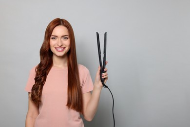 Photo of Beautiful woman with hair iron on light gray background, space for text