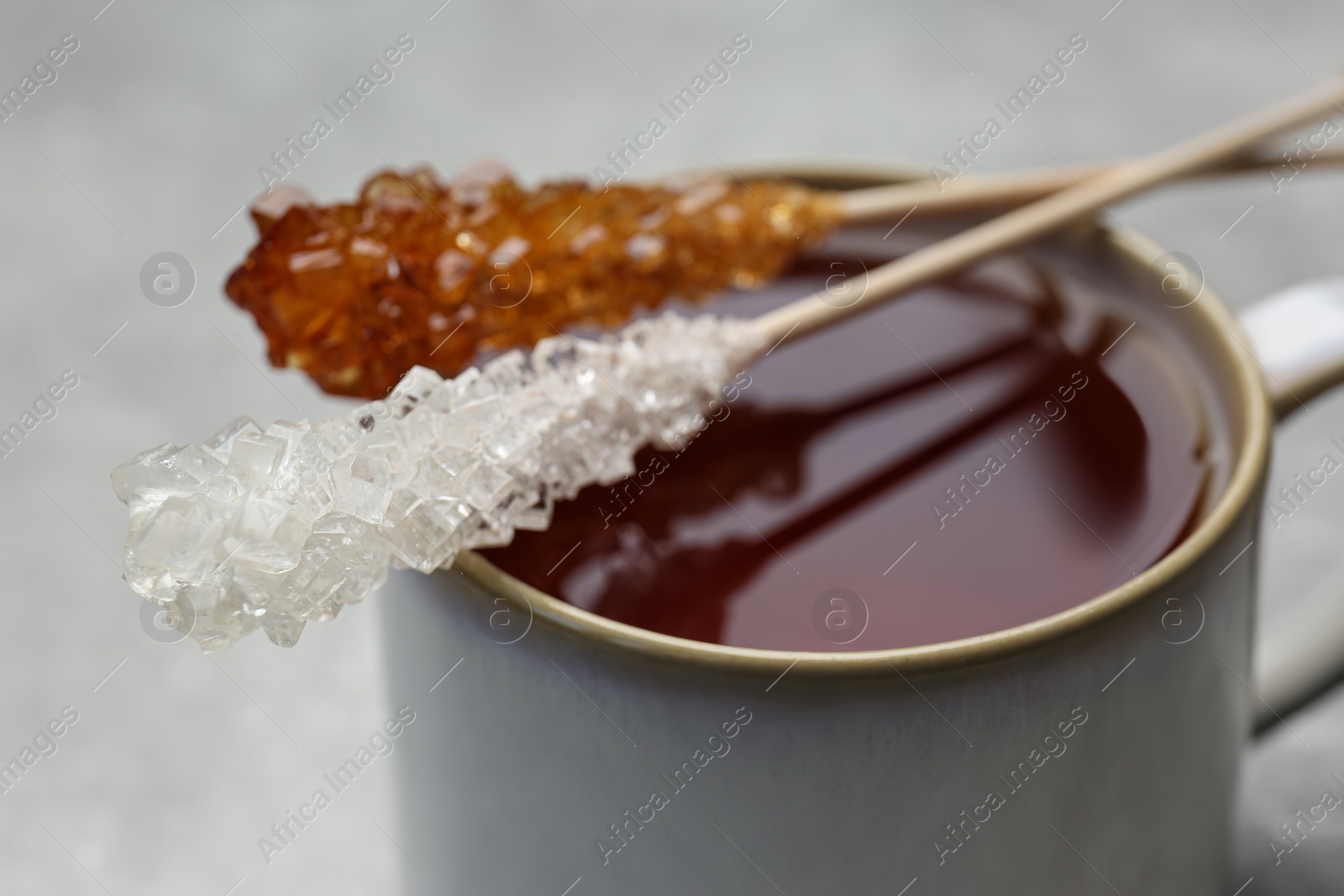 Photo of Sticks with sugar crystals and cup of tea on table, closeup