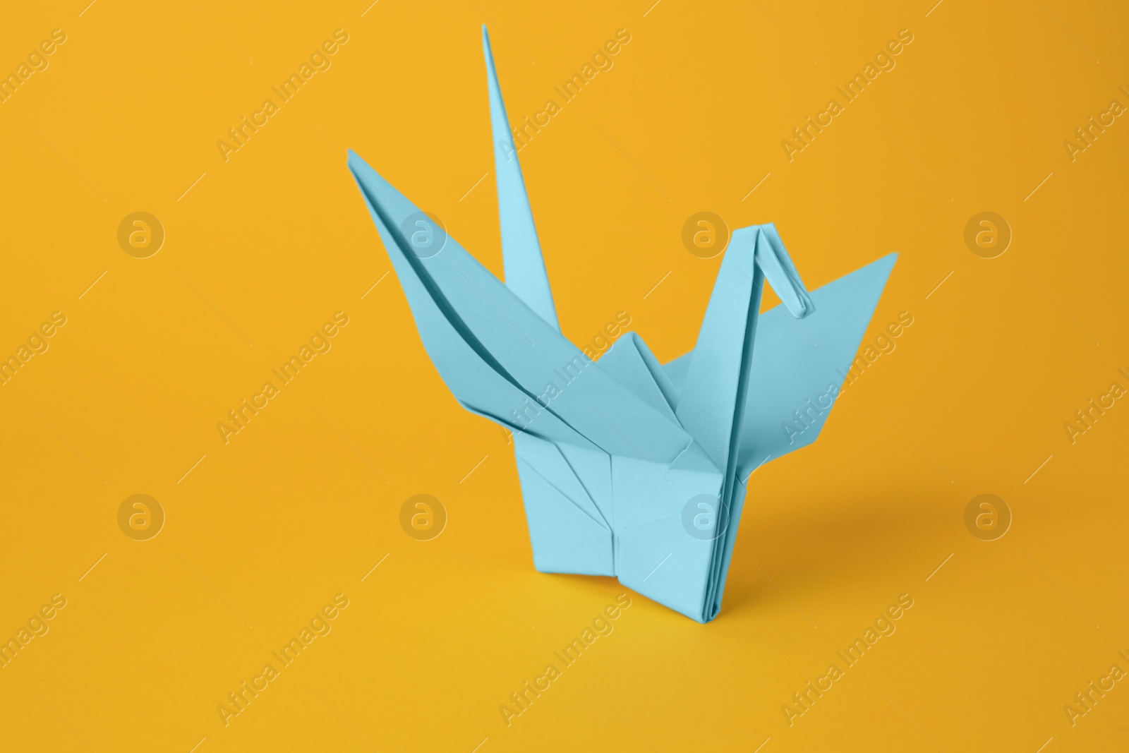 Photo of Origami art. Beautiful light blue paper crane on orange background