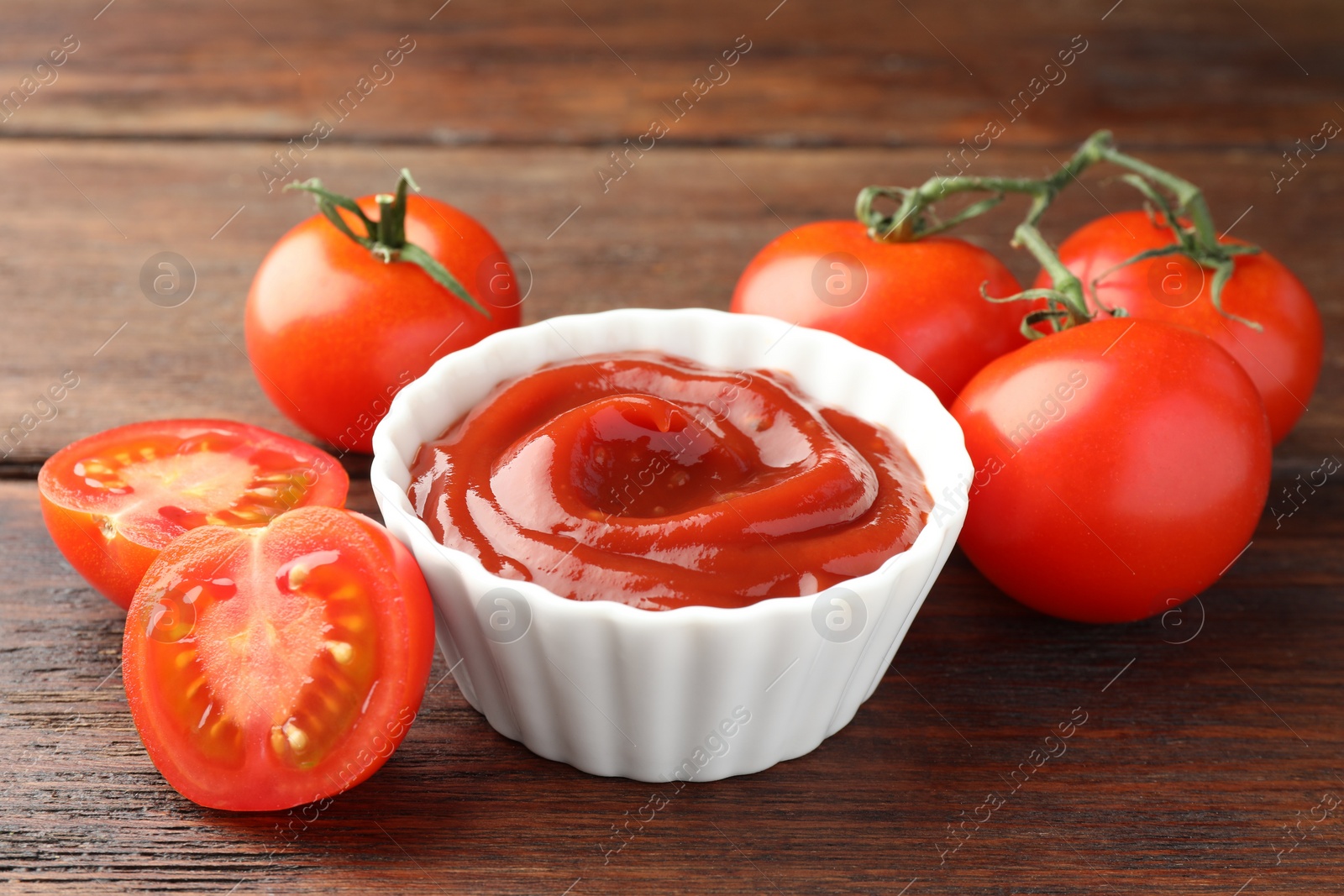 Photo of Bowl of tasty ketchup and tomatoes on wooden table, closeup