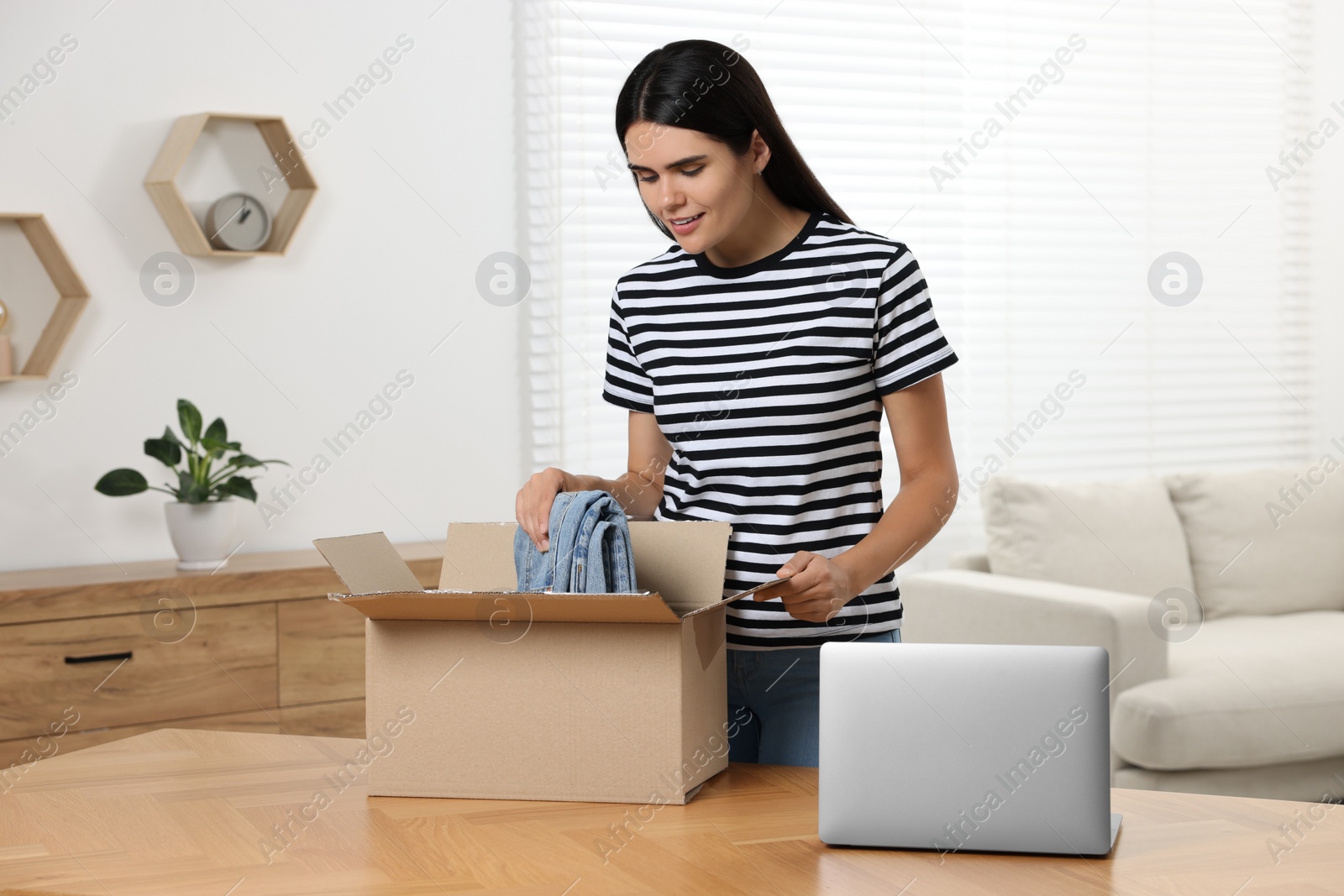 Photo of Young woman with just unpacked new jeans at wooden table indoors. Online shopping