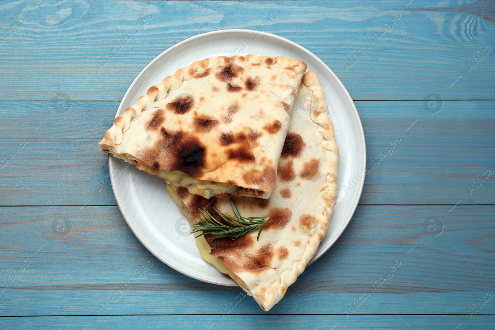 Photo of Tasty pizza calzones with cheese and rosemary on light blue wooden table, top view