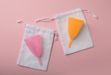 Photo of Menstrual cups with cotton bags on pink background, flat lay