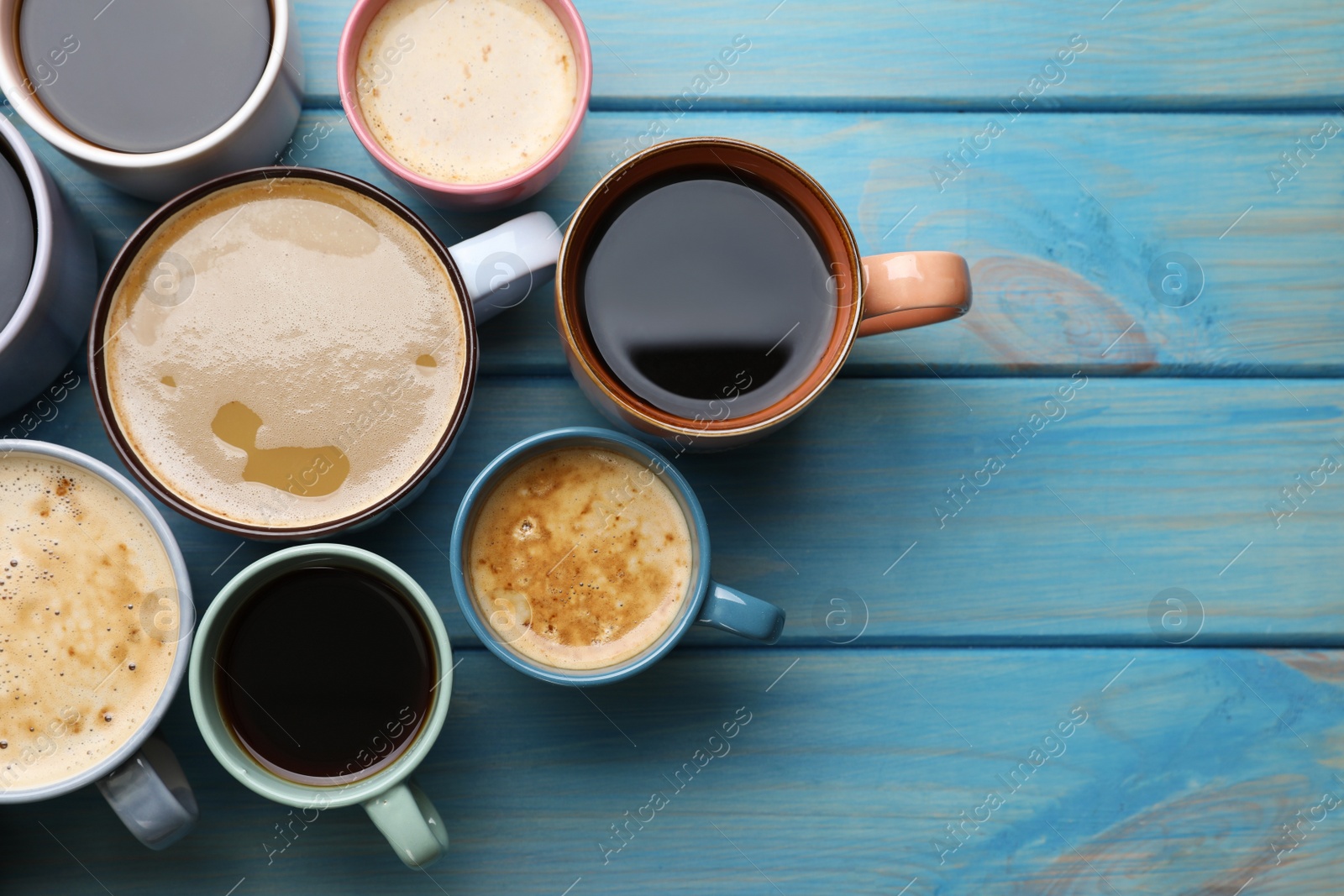 Photo of Many cups of different coffee drinks on light blue wooden table, flat lay. Space for text