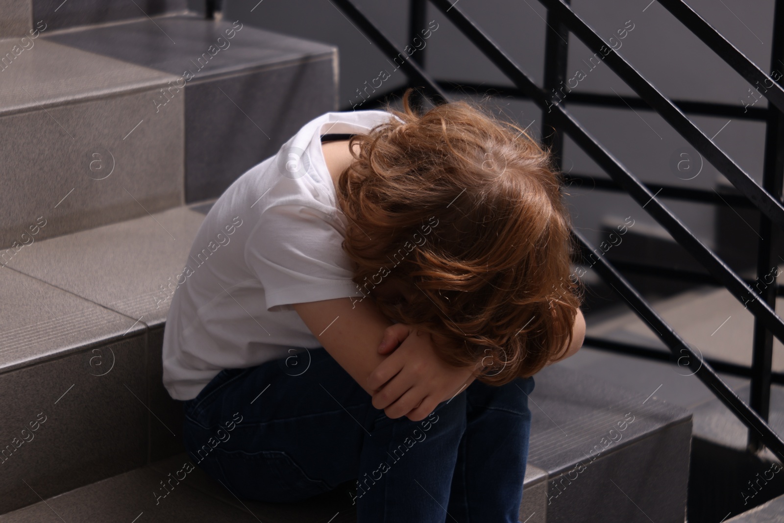 Photo of Child abuse. Upset boy sitting on stairs