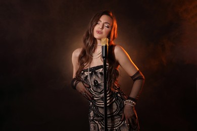 Photo of Beautiful young woman in stylish dress with microphone singing on dark background with smoke