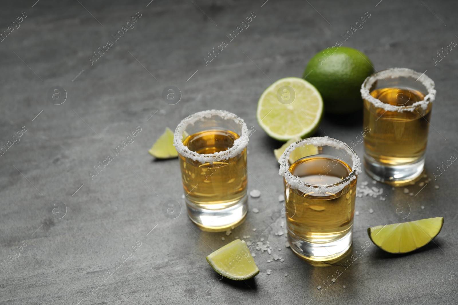 Photo of Mexican Tequila shots, lime slices and salt on grey table