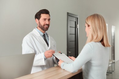 Photo of Happy doctor with clipboard consulting patient in clinic