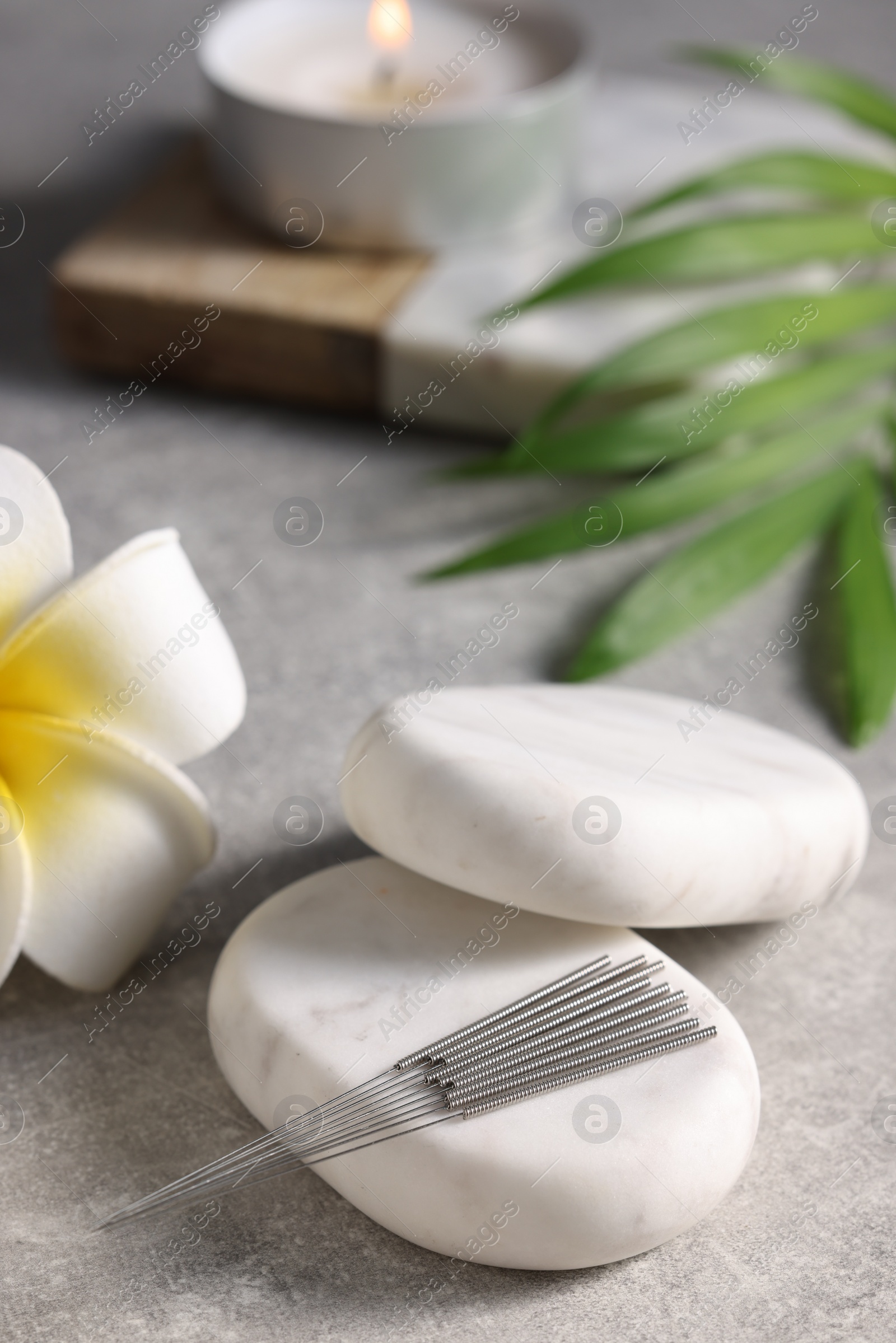 Photo of Stones with acupuncture needles and lily flower on grey table