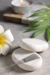 Stones with acupuncture needles and lily flower on grey table