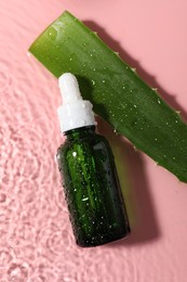 Bottle of cosmetic product and aloe leaf in water on pink background, flat lay