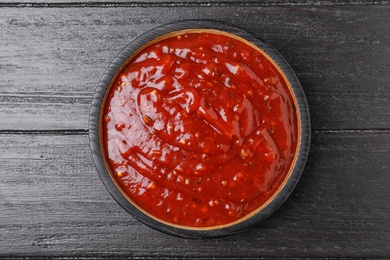 Photo of Bowl of hot chili sauce on dark wooden background, top view
