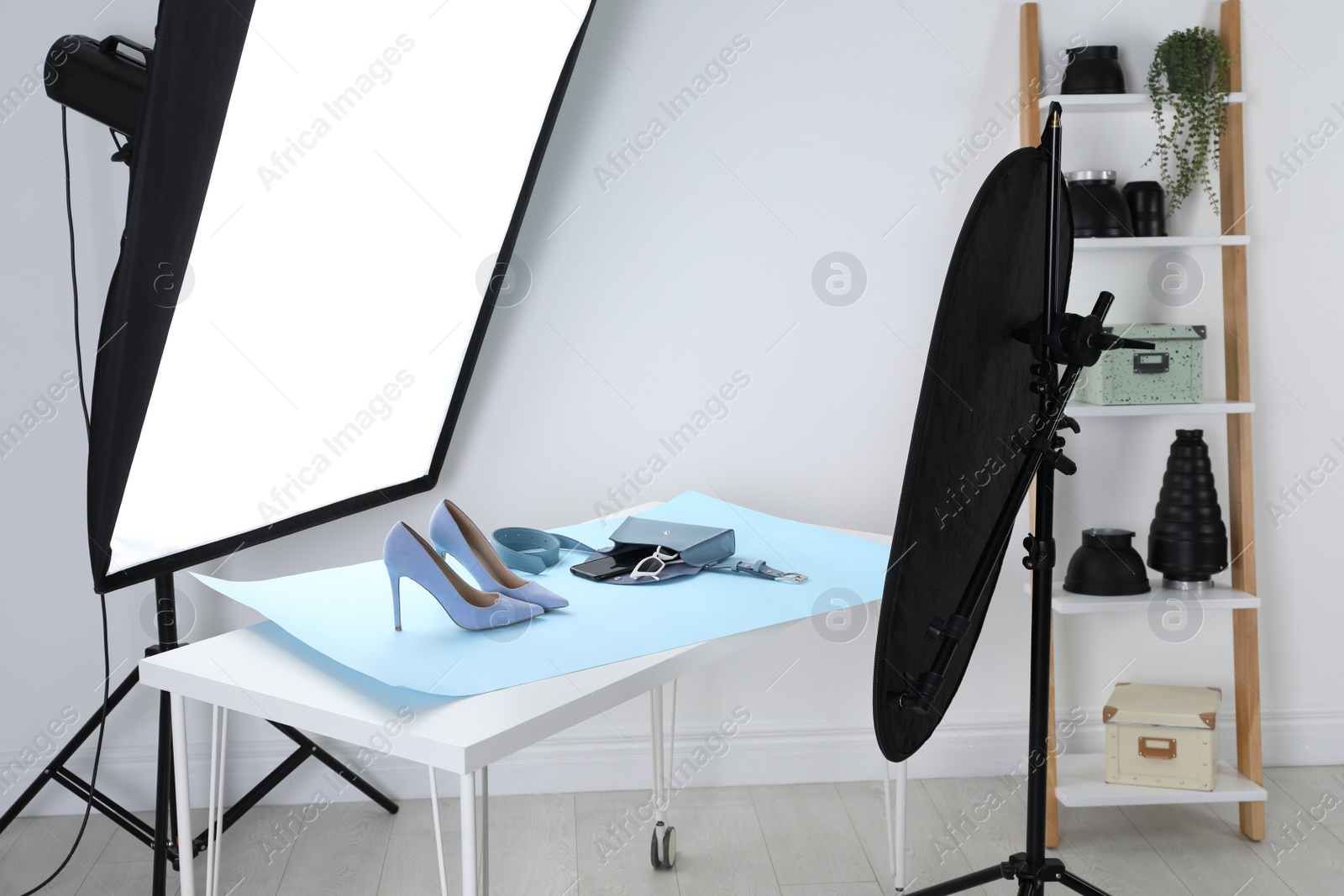 Photo of Professional lighting equipment near table with fashionable women's shoes and accessories in photo studio