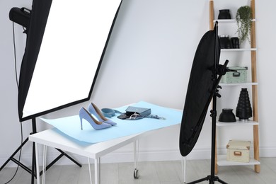 Professional lighting equipment near table with fashionable women's shoes and accessories in photo studio