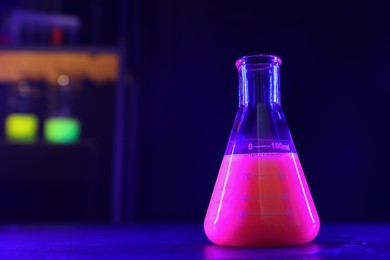 Flask with luminous liquid on table in laboratory, space for text