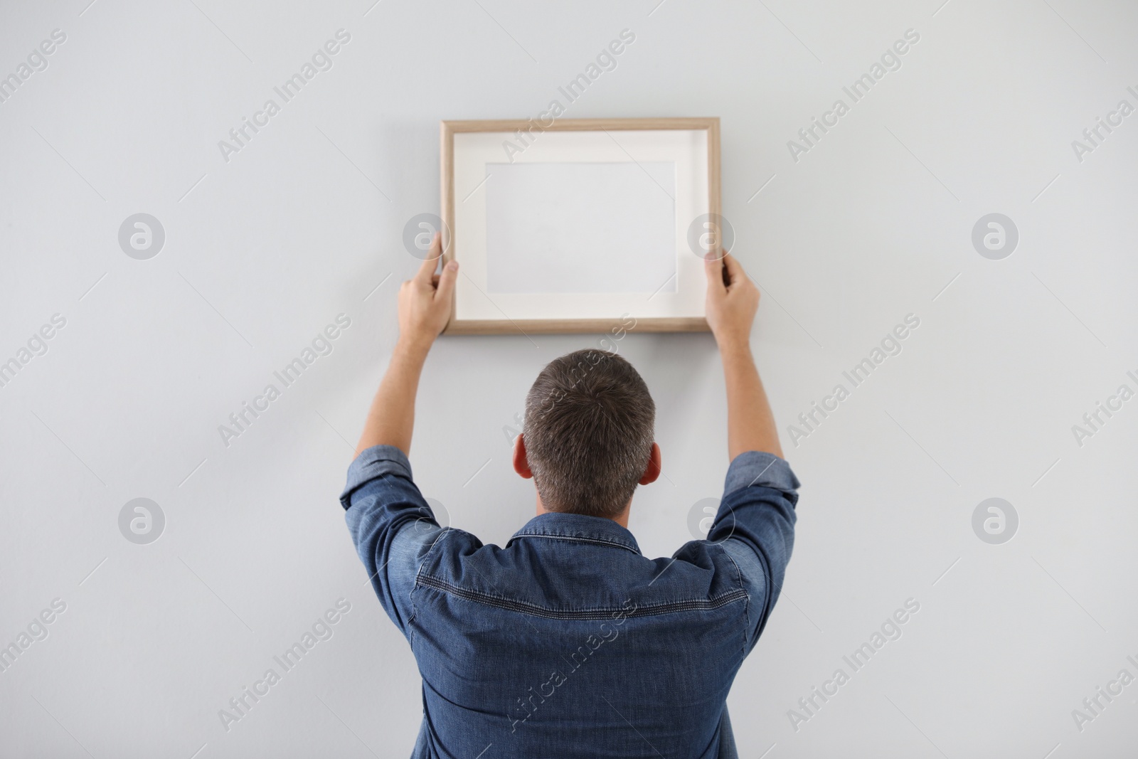 Photo of Man hanging picture on white wall indoors. Interior decoration