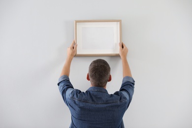 Photo of Man hanging picture on white wall indoors. Interior decoration