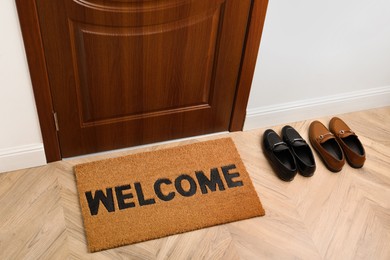 Photo of New clean brown mat with word Welcome and shoes near entrance door