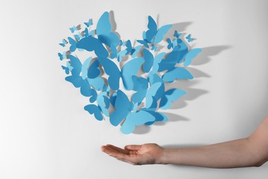 Image of Light blue paper butterflies on white wall. Woman showing decorative element