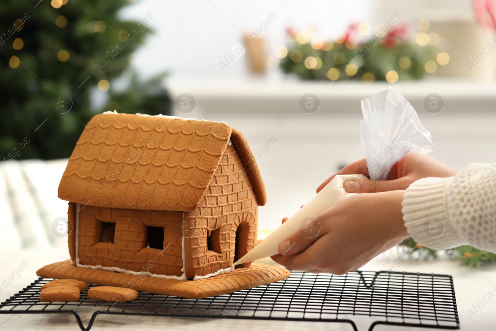 Photo of Woman making gingerbread house at table indoors, closeup