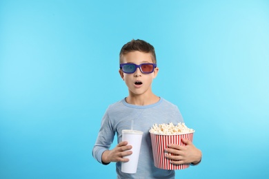 Emotional boy with 3D glasses, popcorn and beverage during cinema show on color background