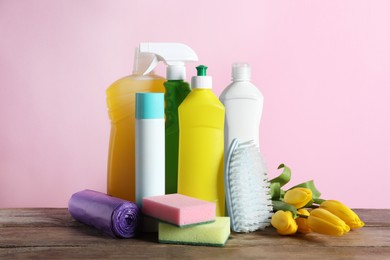 Photo of Spring cleaning. Detergents, tools and flowers on wooden table against pink background