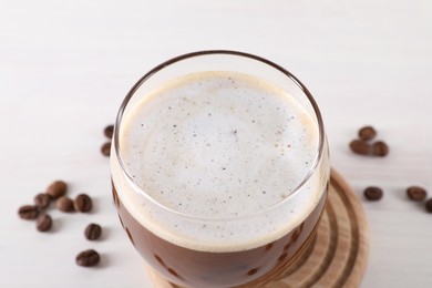 Photo of Refreshing iced coffee with milk in glass and beans on white table, closeup